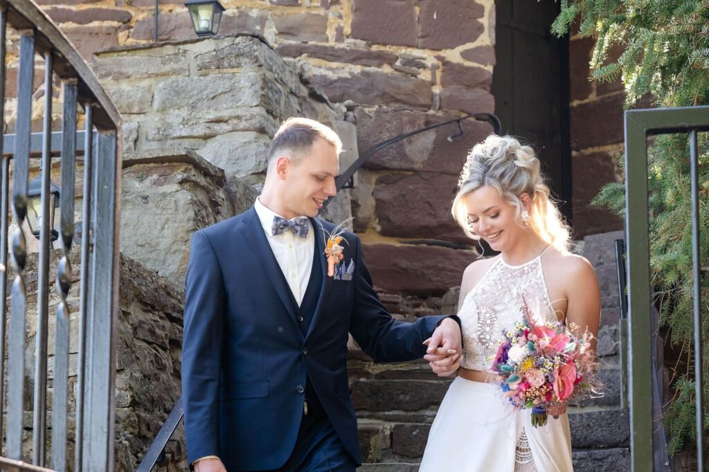 Brautpaar vor einer alten Burgmauer mit Blumenstrauß