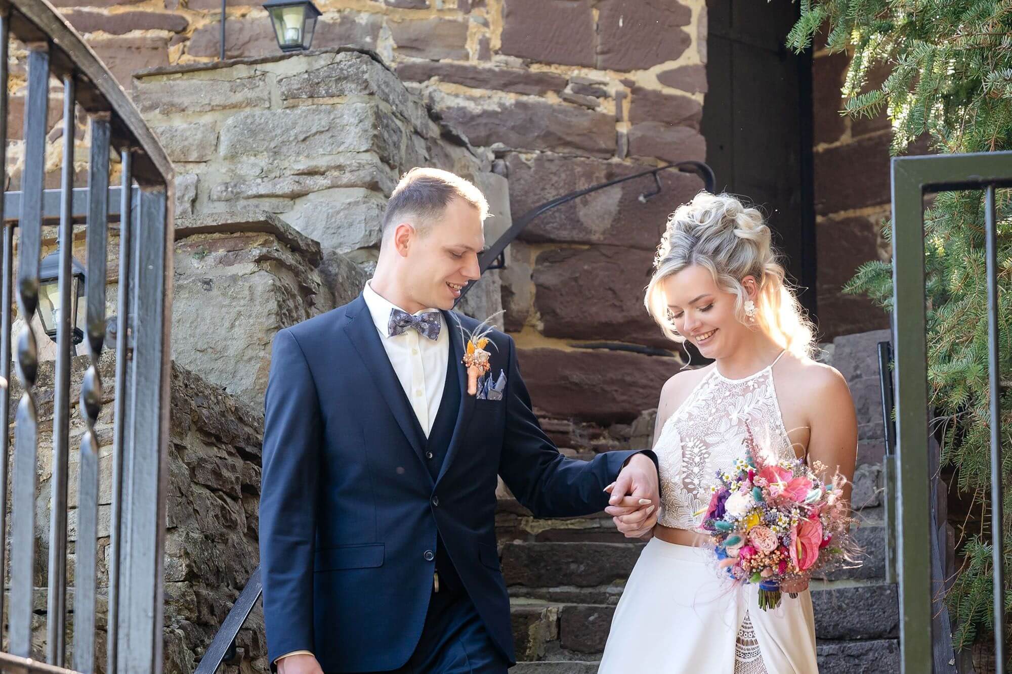 Brautpaar vor einer alten Burgmauer mit Blumenstrauß