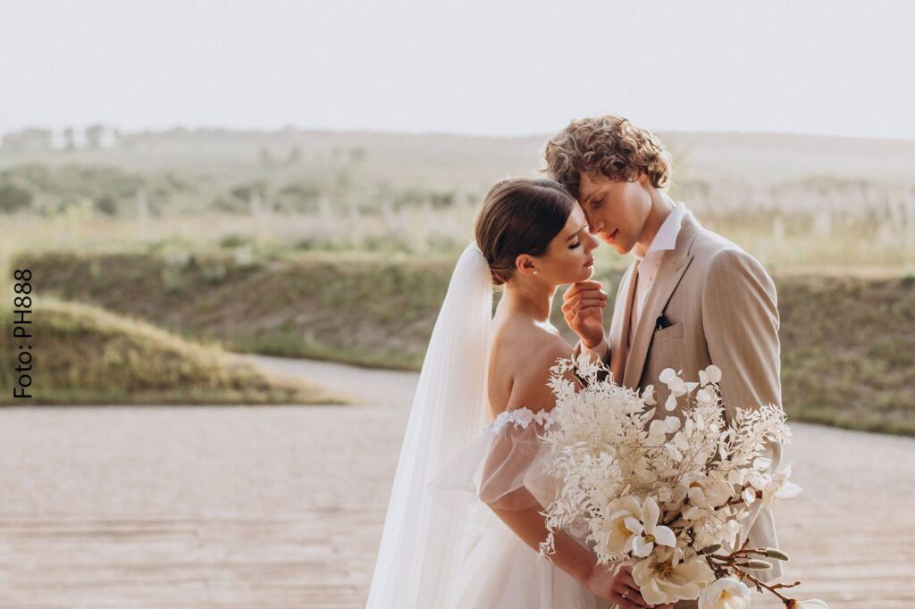 Brautpaar umgeben von einer Naturkulisse, mit Blumenstrauß in der Hand